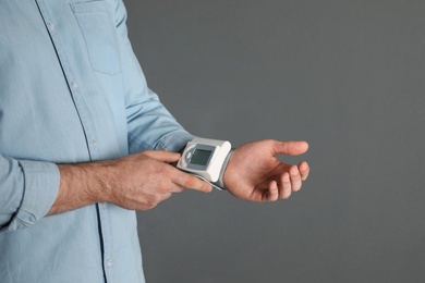 Young man checking pulse with digital medical device on grey background, closeup. Space for text