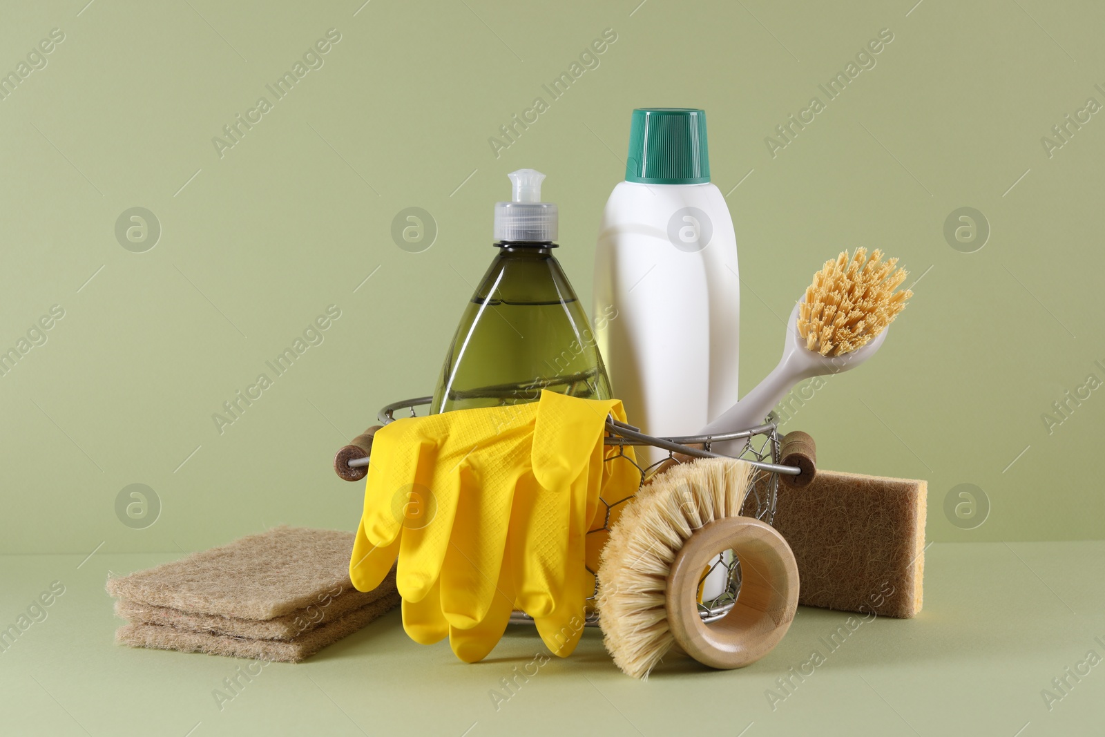 Photo of Set of different cleaning supplies in basket on light green background