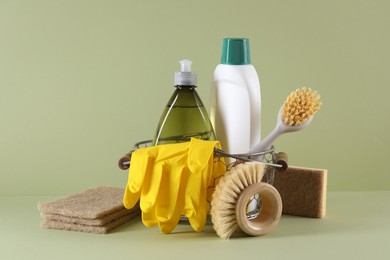 Photo of Set of different cleaning supplies in basket on light green background