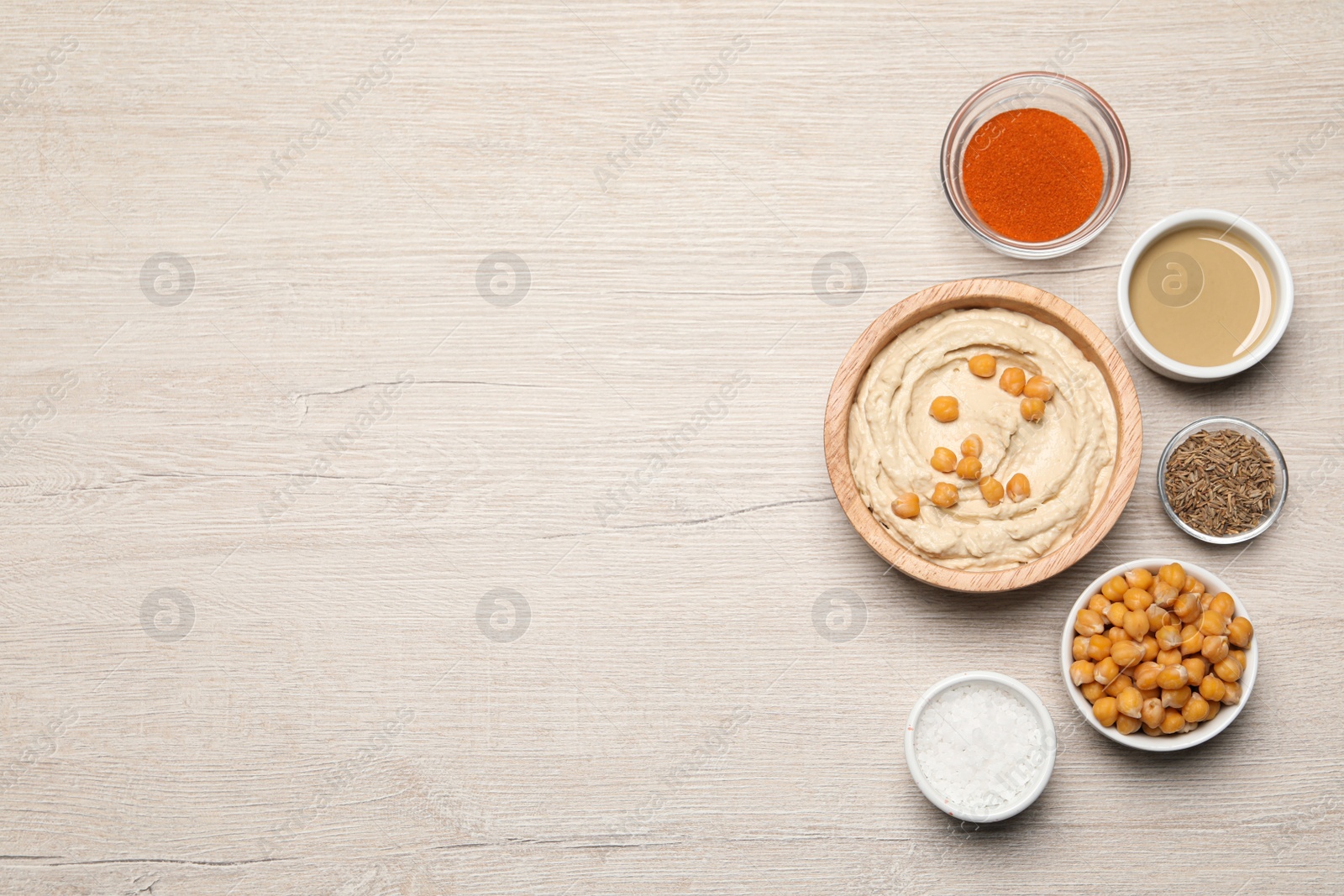 Photo of Bowl with delicious hummus and different ingredients on white wooden table, flat lay. Space for text