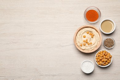 Photo of Bowl with delicious hummus and different ingredients on white wooden table, flat lay. Space for text
