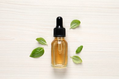 Photo of Glass bottle of basil essential oil and leaves on white  wooden table, flat lay