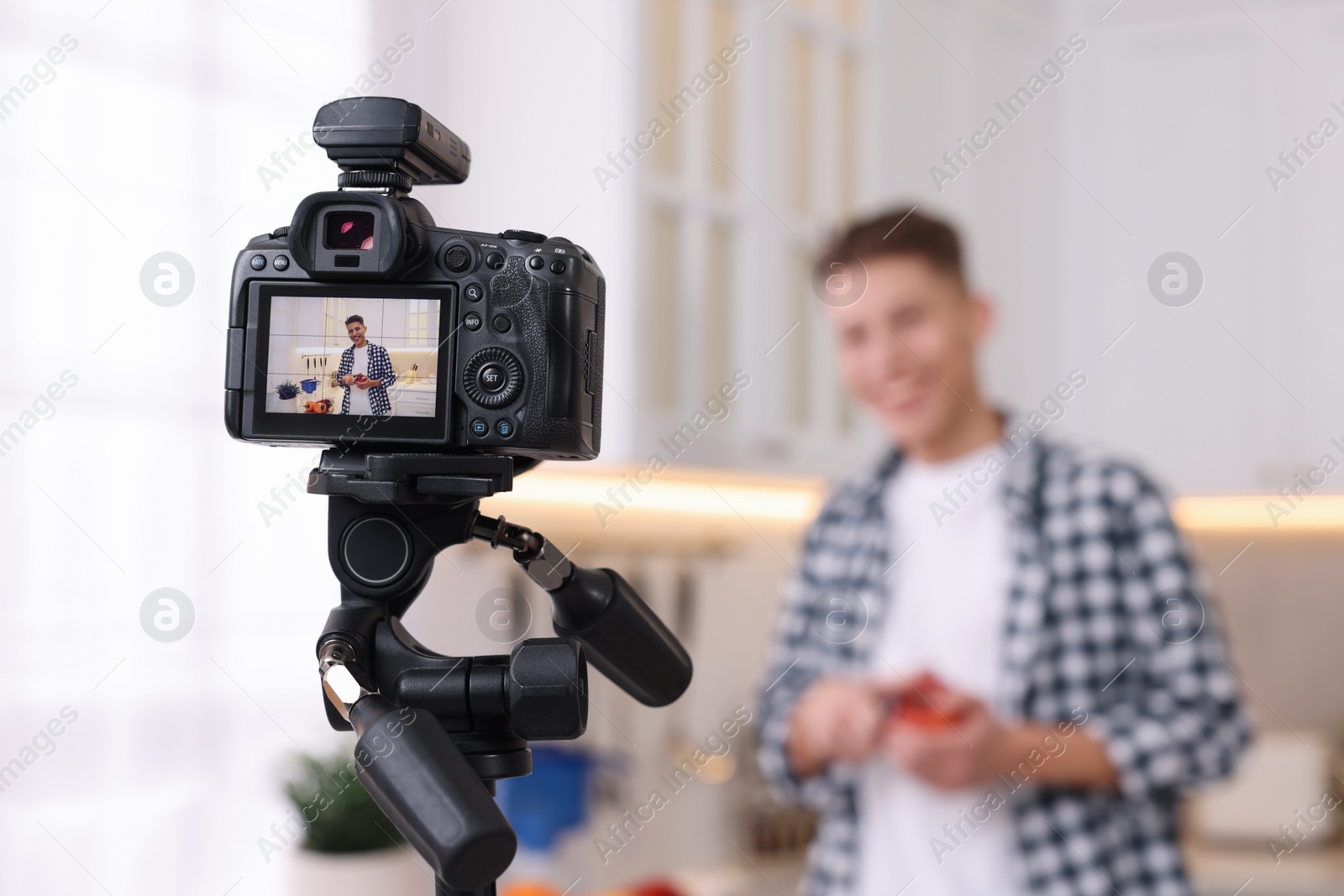 Photo of Food blogger recording video in kitchen, focus on camera