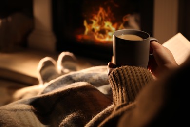 Photo of Woman with cup of drink near fireplace at home, closeup