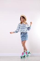 Young woman with retro roller skates near white wall