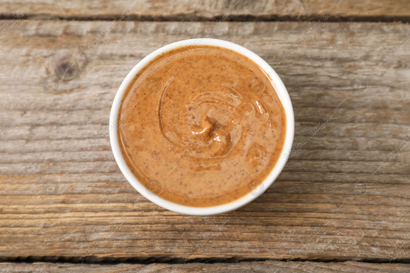 Photo of Delicious nut butter in bowl on wooden table, top view