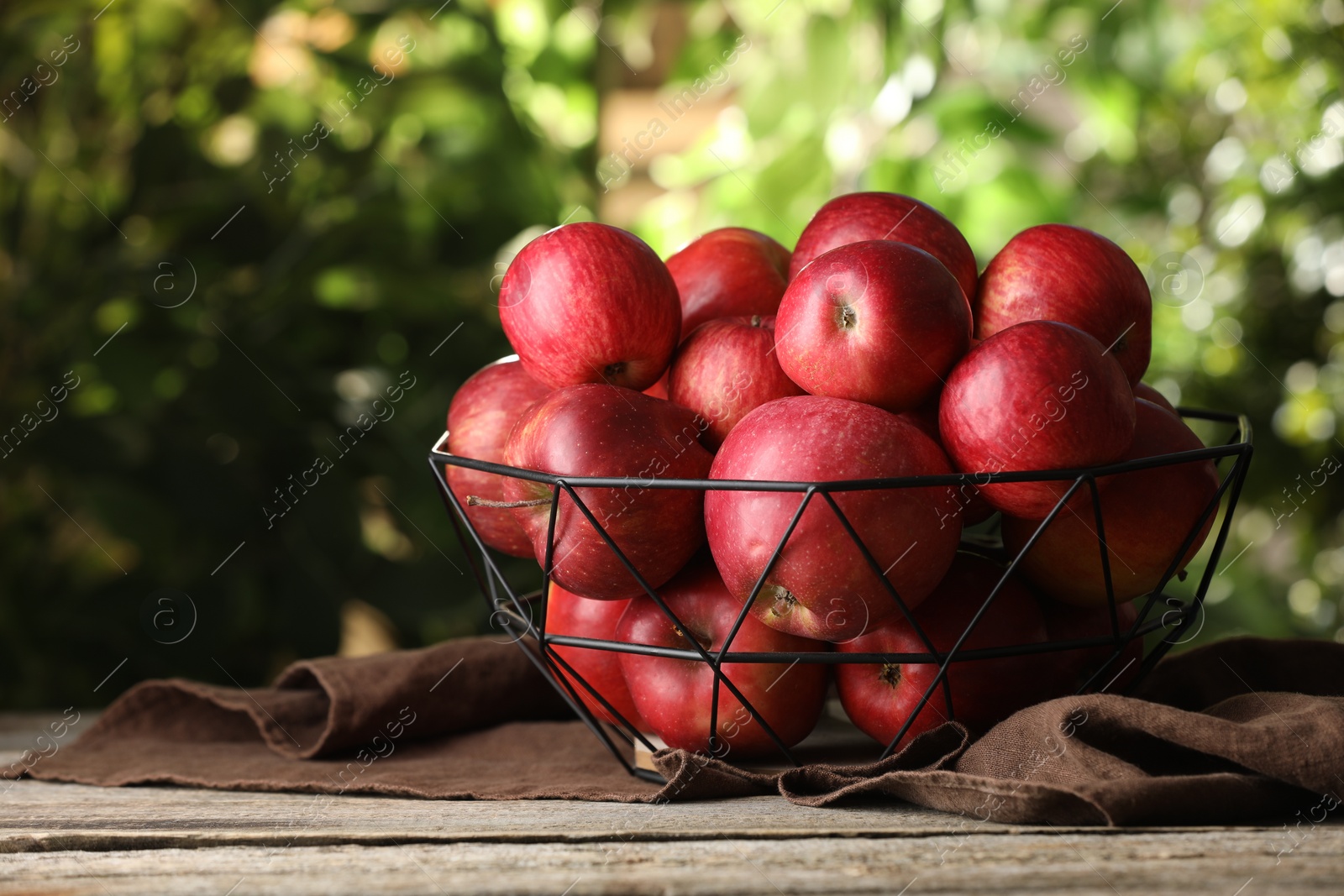 Photo of Ripe red apples in bowl on wooden table outdoors