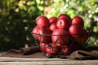 Photo of Ripe red apples in bowl on wooden table outdoors