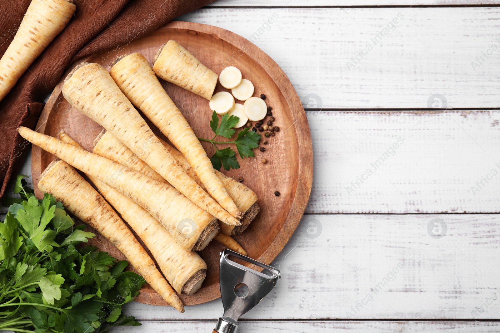 Photo of Raw parsley roots and bunch of fresh herb on white wooden table, flat lay. Space for text