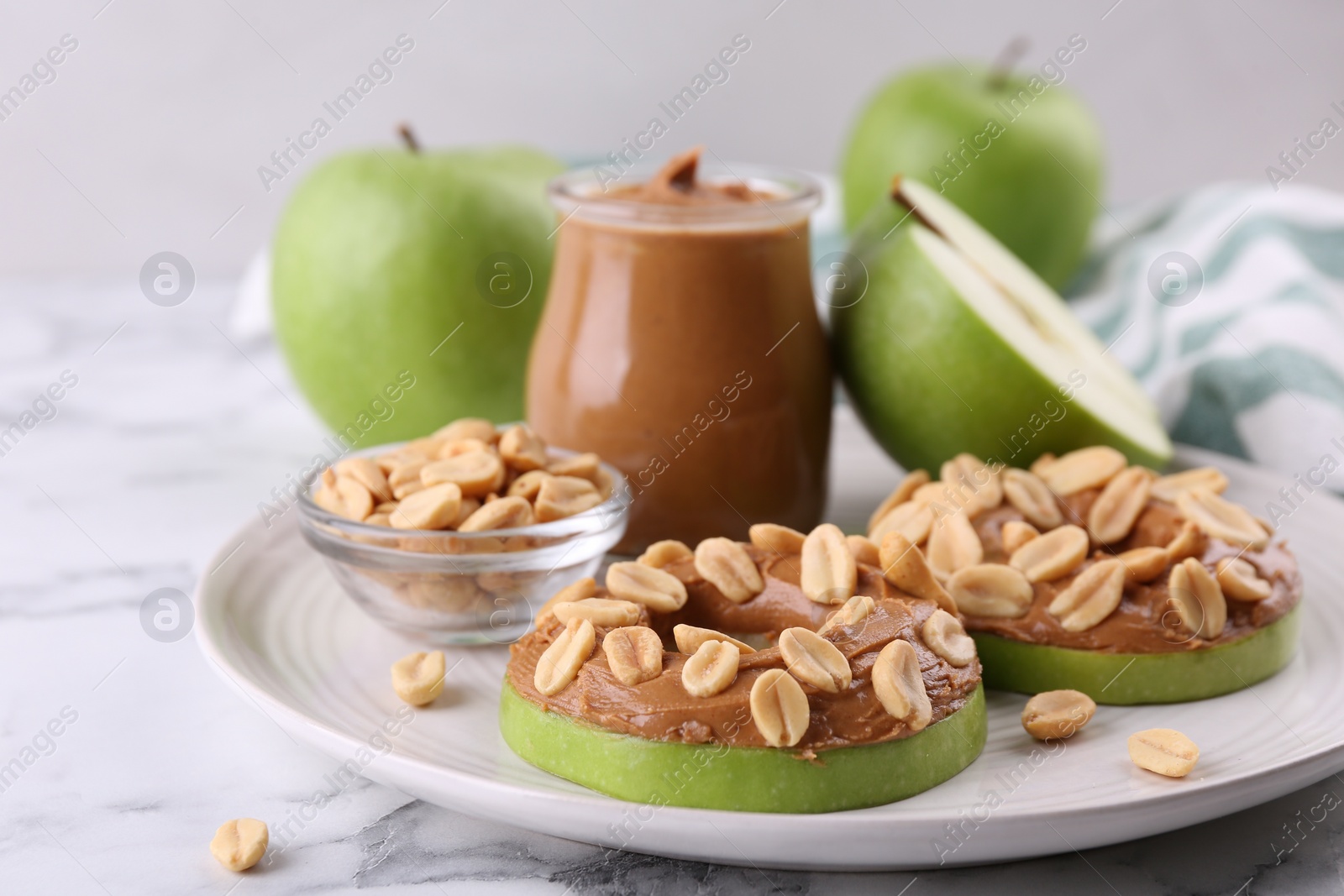 Photo of Fresh green apples with peanut butter and nuts on white marble table, closeup