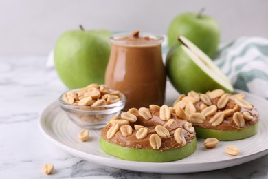 Photo of Fresh green apples with peanut butter and nuts on white marble table, closeup