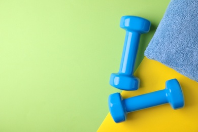 Vinyl dumbbells and towel on color background, flat lay. Space for text