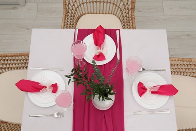 Table setting. Glasses of tasty beverage, plates, pink napkins and vase with green branches in dining room, above view