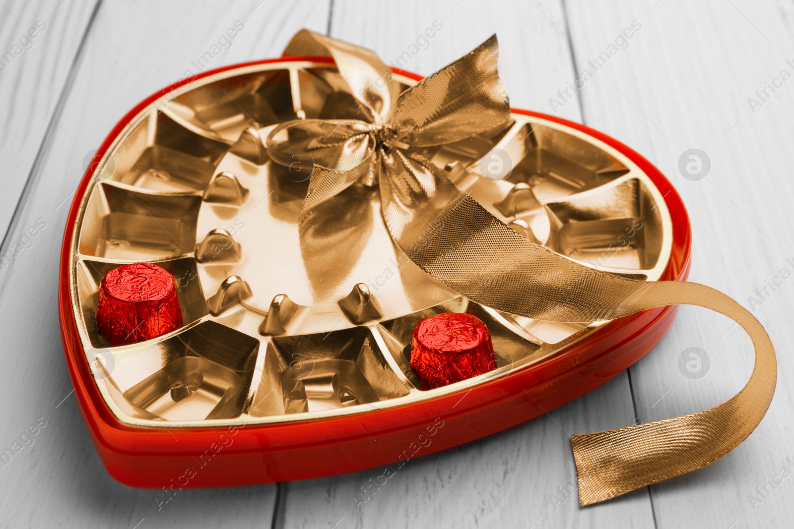 Photo of Partially empty box of chocolate candies on white wooden table, closeup