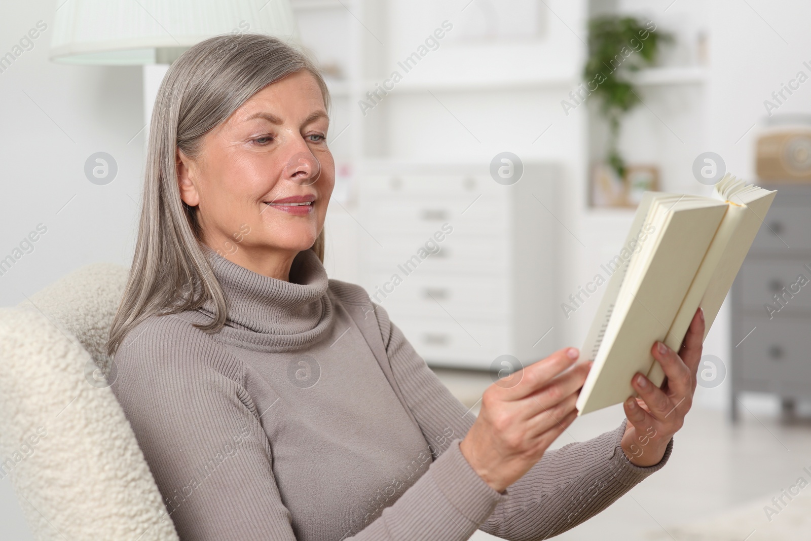 Photo of Beautiful senior woman reading book in armchair at home