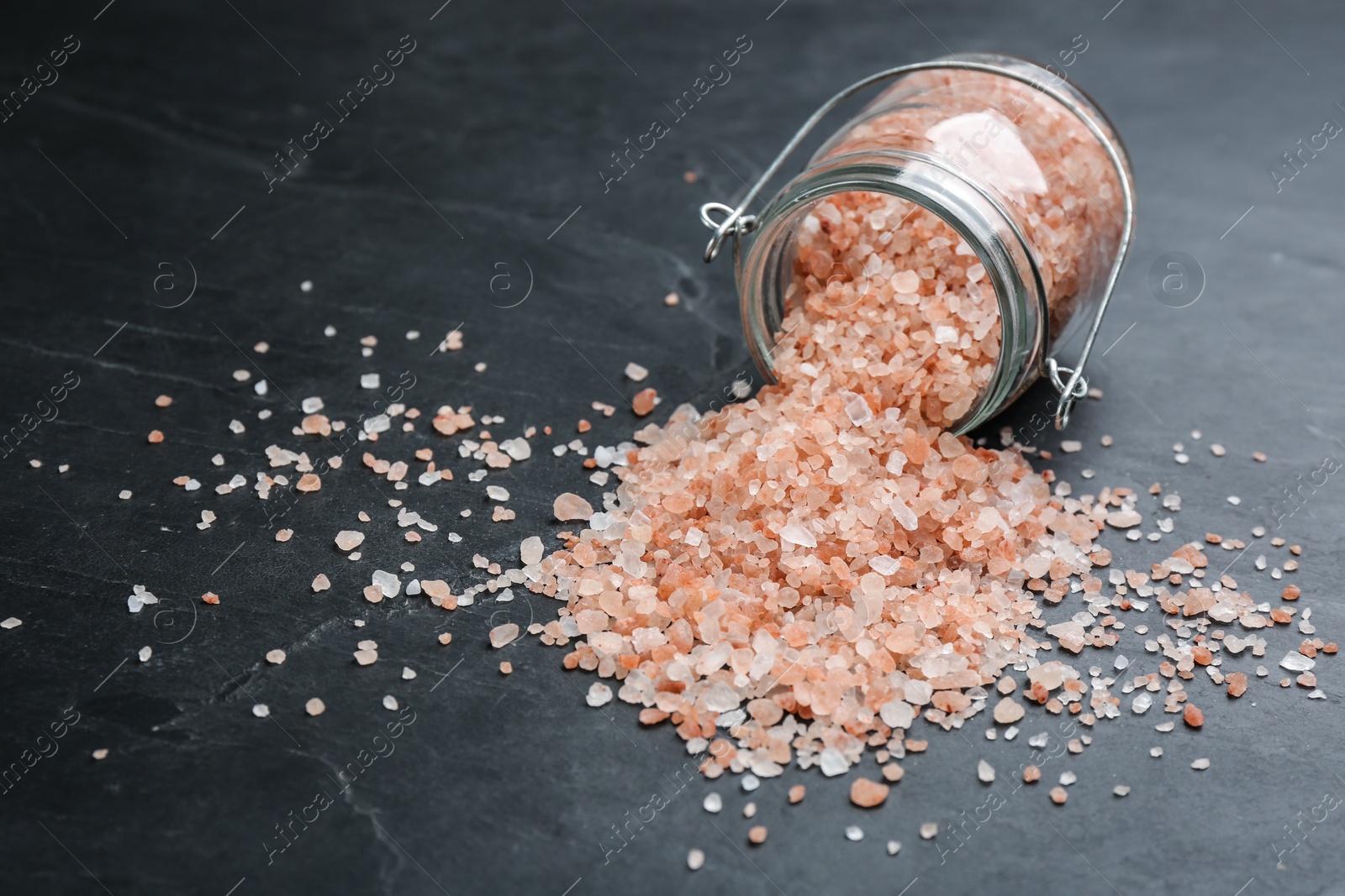 Photo of Overturned glass jar with pink himalayan salt on black table