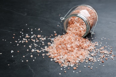 Photo of Overturned glass jar with pink himalayan salt on black table