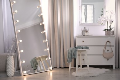 Large mirror with light bulbs and chest of drawers in stylish room. Interior design