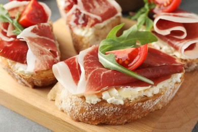 Tasty sandwiches with cured ham, tomatoes and arugula on wooden board, closeup