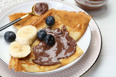 Tasty crepes with chocolate paste, blueberries and banana served on white wooden table, closeup