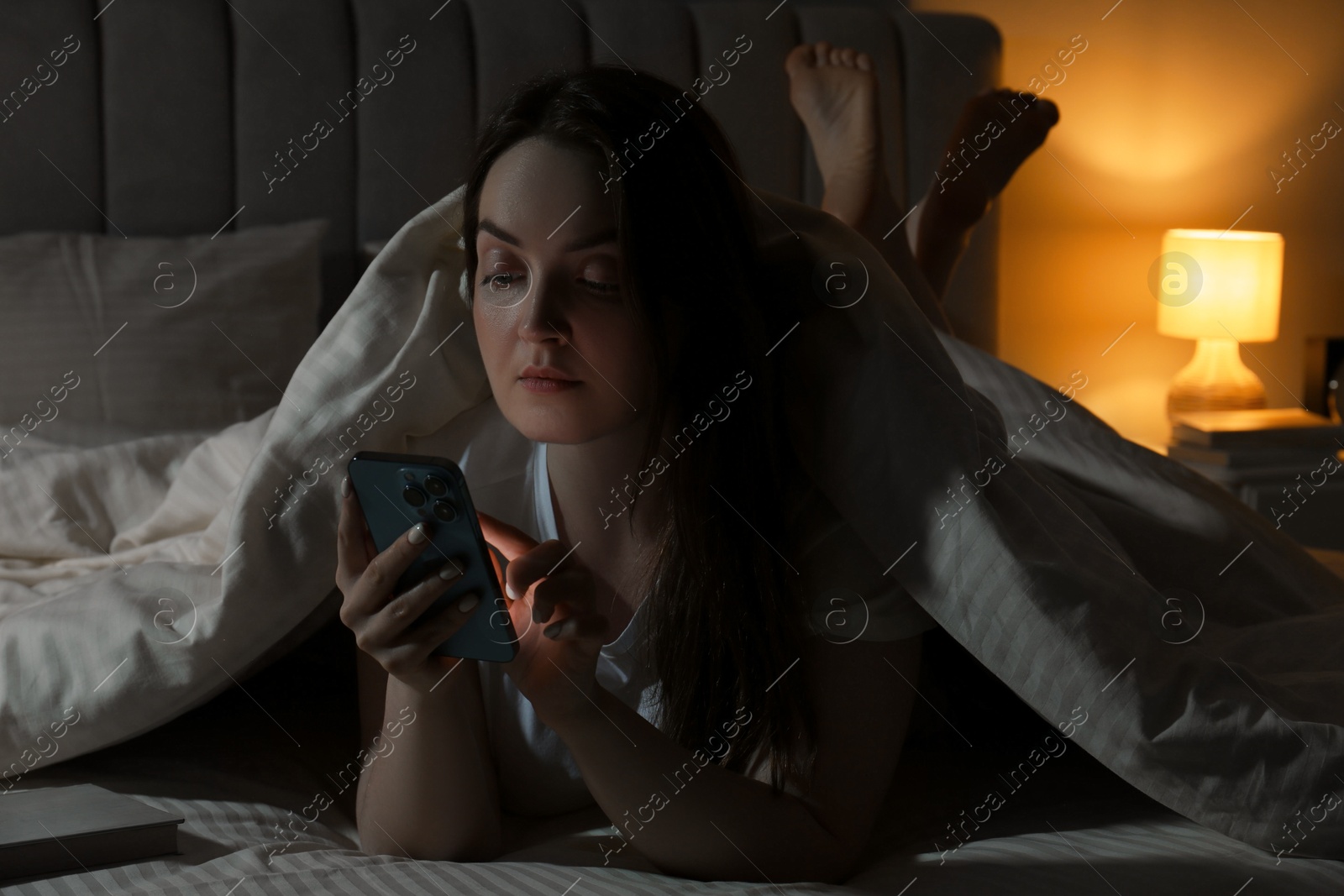 Photo of Woman using smartphone in bed at night. Internet addiction