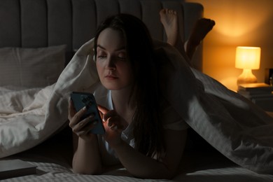 Woman using smartphone in bed at night. Internet addiction