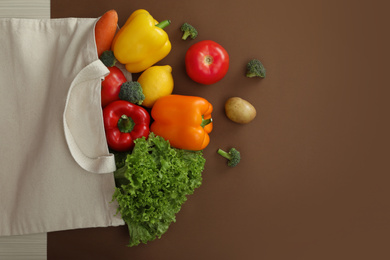 Photo of Eco bag with fruits and vegetables on brown background, flat lay. Space for text