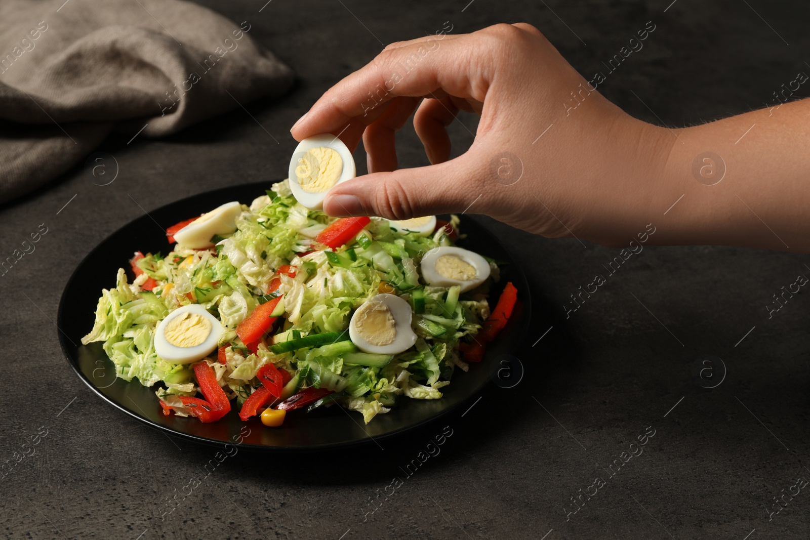 Photo of Woman making delicious salad with Chinese cabbage and quail eggs at black table, closeup