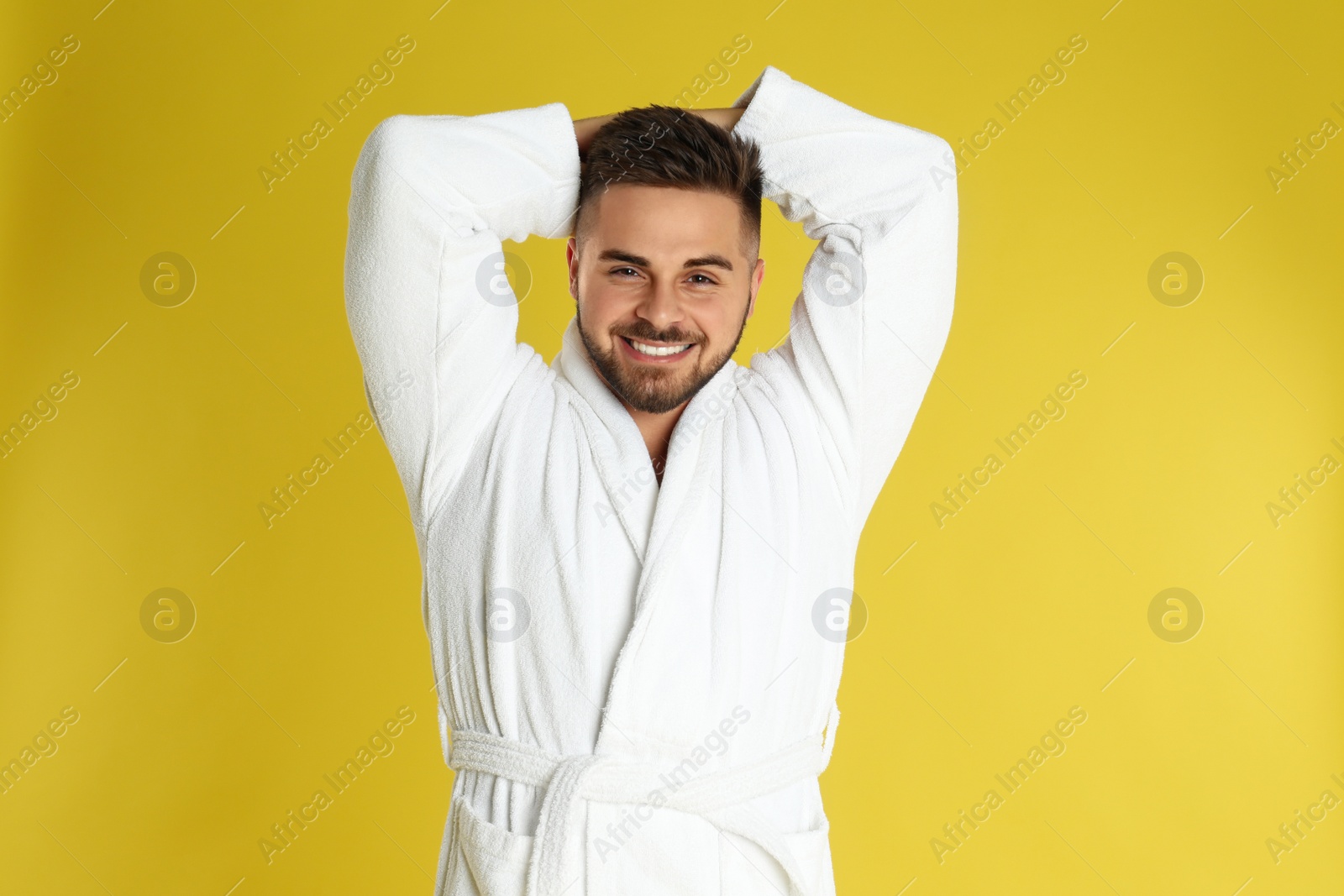 Photo of Happy young man in bathrobe on yellow background