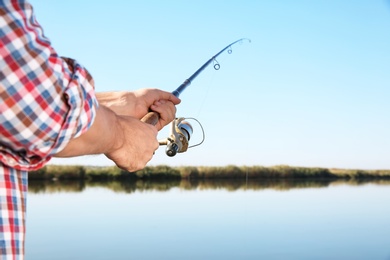 Photo of Man fishing alone at riverside on sunny day, closeup. Space for text