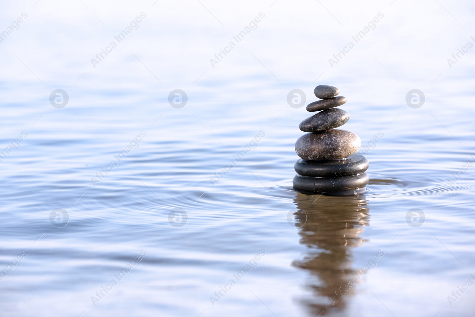 Photo of Stack of dark stones in sea water, space for text. Zen concept