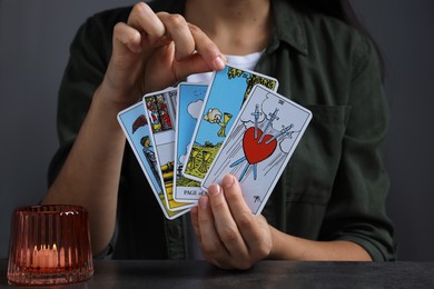 Photo of Fortune teller with tarot cards at grey table indoors, closeup