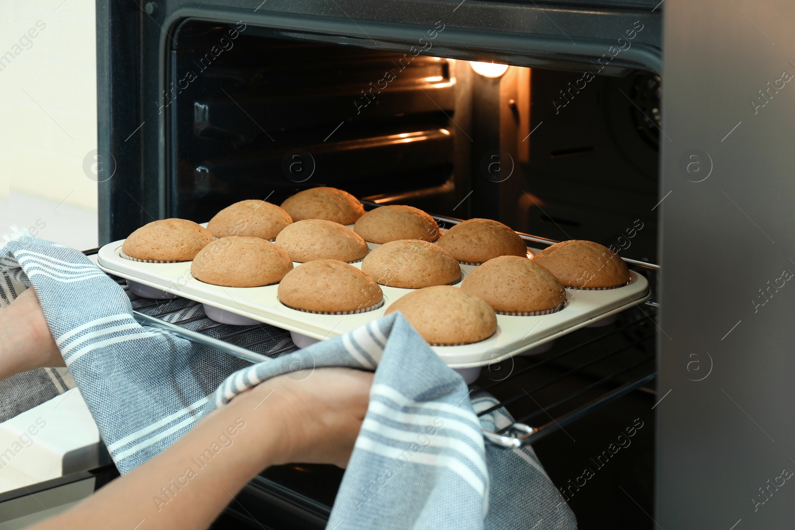 Photo of Woman taking cupcakes out of oven indoors, closeup