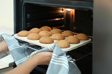 Photo of Woman taking cupcakes out of oven indoors, closeup