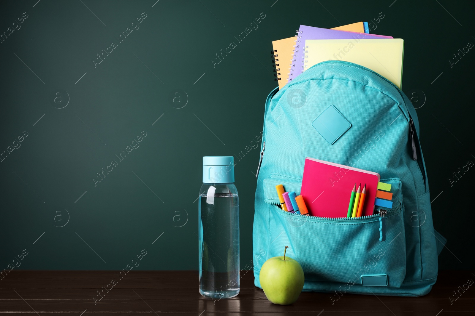 Photo of Backpack with different school stationery on wooden table near chalkboard, space for text