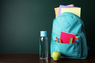 Photo of Backpack with different school stationery on wooden table near chalkboard, space for text