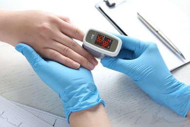 Photo of Doctor examining patient with fingertip pulse oximeter at white wooden table, closeup