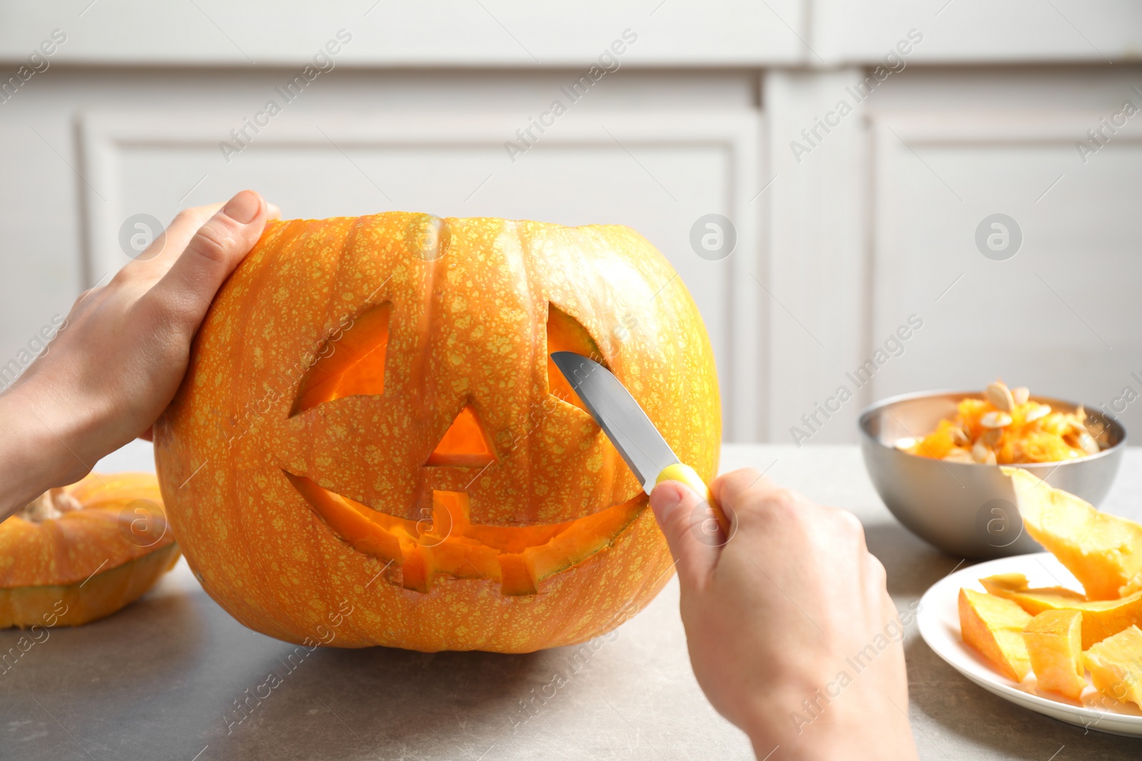 Photo of Woman carving pumpkin head Jack lantern for Halloween at light table indoors, closeup