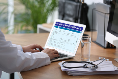 Doctor with modern laptop indoors, closeup. Health insurance