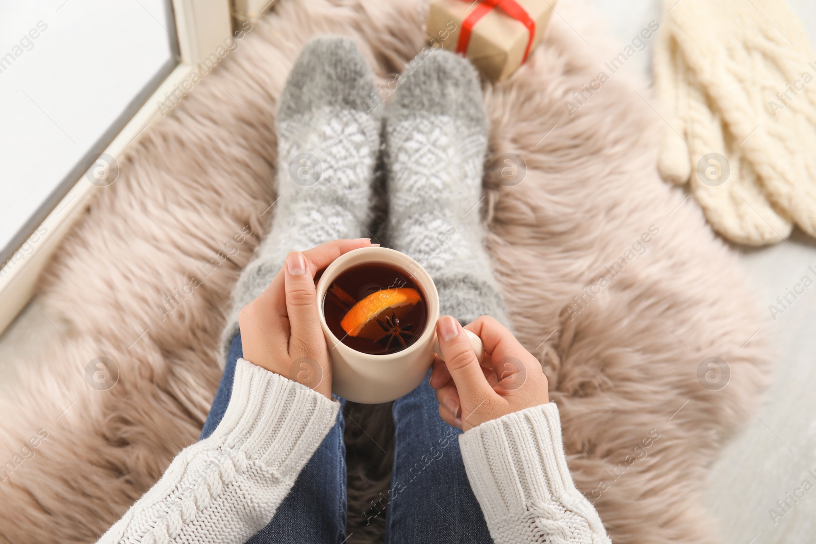 Photo of Woman with cup of hot mulled wine sitting on window sill, above view. Winter drink