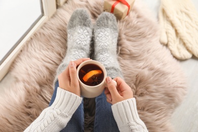 Photo of Woman with cup of hot mulled wine sitting on window sill, above view. Winter drink