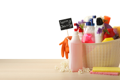 Photo of Spring Cleaning sign, flowers and detergents in basket on wooden table. Space for text