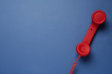 Photo of Red corded telephone handset on blue background, top view. Hotline concept
