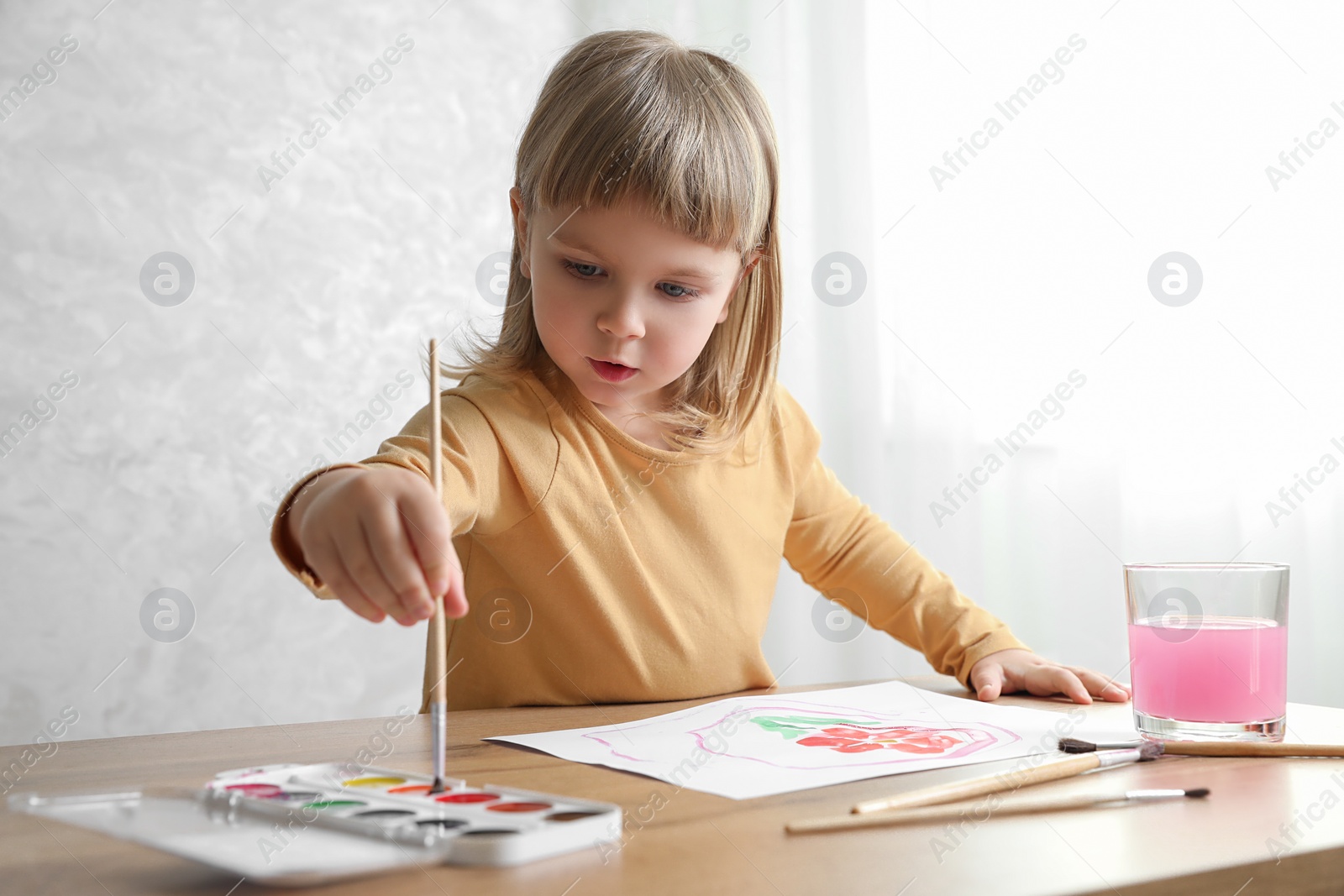 Photo of Cute little girl drawing with brush at wooden table indoors. Child`s art