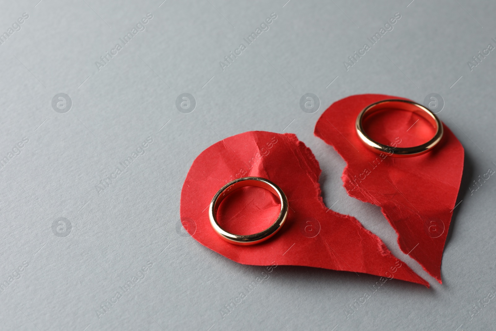 Photo of Halves of torn red paper heart and wedding rings on white background, space for text. Broken heart