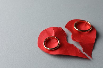 Halves of torn red paper heart and wedding rings on white background, space for text. Broken heart