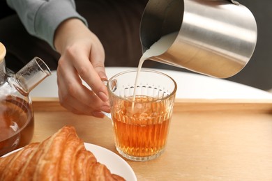 Photo of Woman pouring milk into cup with aromatic tea at table indoors, closeup