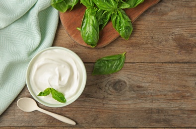 Flat lay composition with sour cream and basil on wooden table, space for text