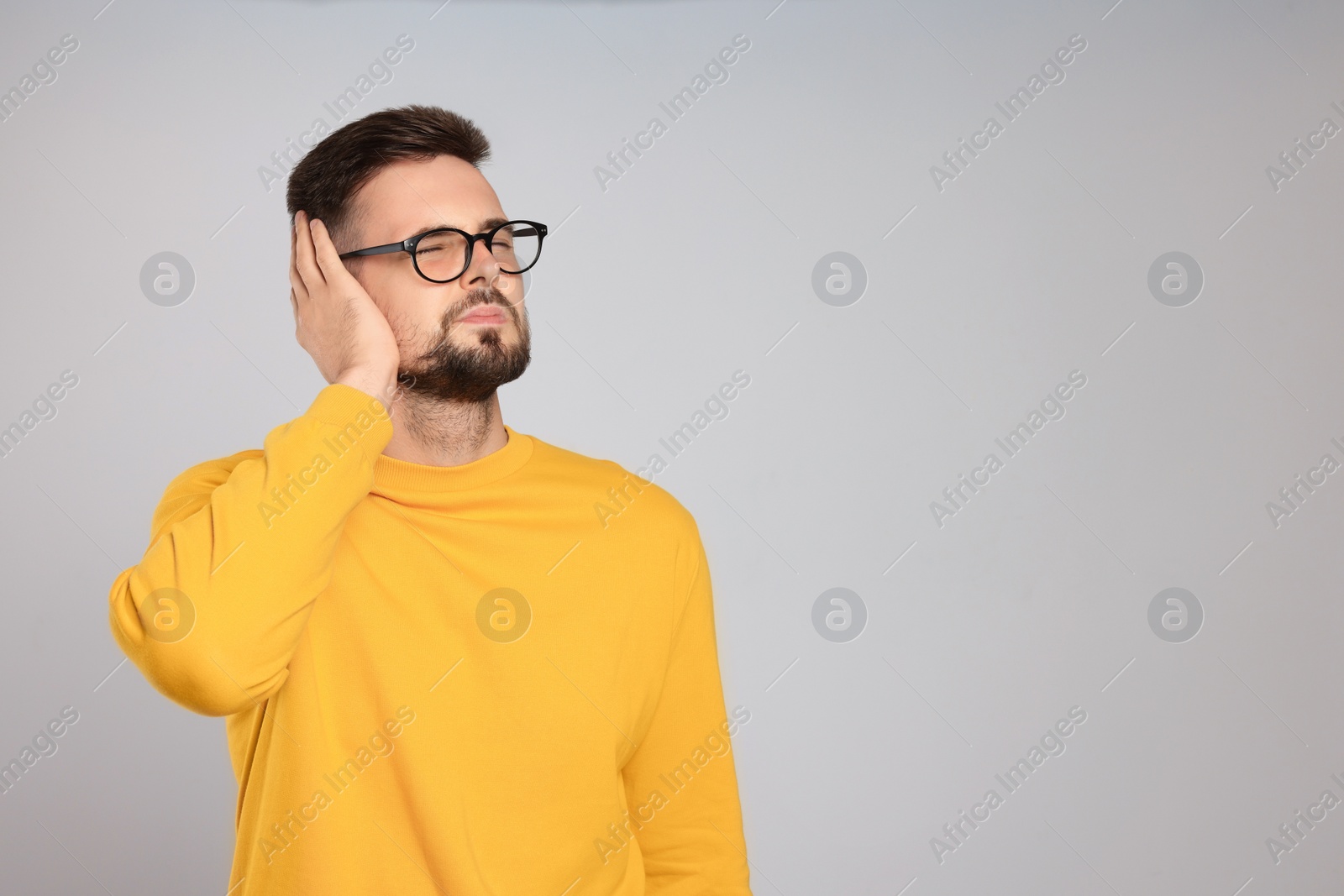 Photo of Young man suffering from ear pain on light grey background. Space for text