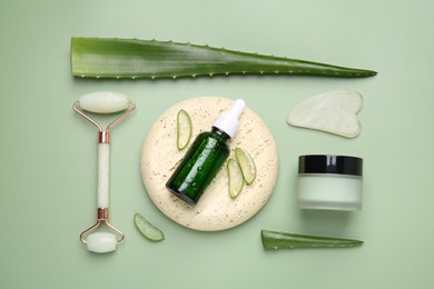 Photo of Flat lay composition with cosmetic products and cut aloe leaves on pale green background